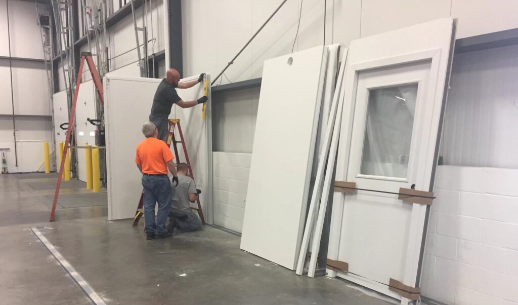 A crew of workers installing a modular building inside of a warehouse.
